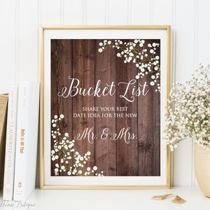 May include: A printable sign with a rustic wood background and white flowers. The sign says "Bucket List" and "Share your best date idea for the new Mr. & Mrs."