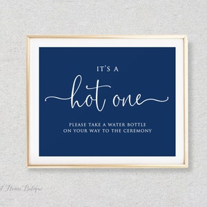 May include: A navy blue sign with white text that reads "It's a hot one. Please take a water bottle on your way to the ceremony."