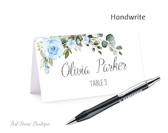 Può includere: Un segnaposto bianco con un design floreale blu e il testo "Olivia Parker, Tavolo 3". Una penna nera è appoggiata accanto al segnaposto.