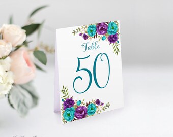 May include: White table number card with teal and purple floral design. The card says "Table 50" in a teal script font.