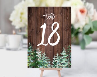 Op de afbeelding: Een rustiek houten tafelnummerbord met het nummer 18 in witte tekst. Het bord heeft een houtnerf achtergrond en een groene aquarel bos scène aan de onderkant.