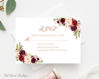 May include: A white RSVP card with a floral design in shades of burgundy, pink, and green. The text "RSVP" is written in a cursive font in a light pink color. The text "Kindly respond by April 24, 2021" is printed below the floral design. The card has three lines for guests to indicate their response: "Happily Accepts", "Regretfully Declines", and "Number of Guests Attending".