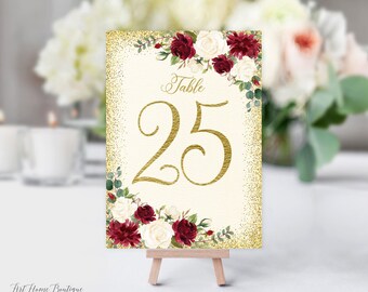 Könnte beinhalten: Tischnummer 25 mit goldfarbenem Glitzerhintergrund und burgunderrotem und weißem Blumendesign. Die Tischnummer ist in goldener Schrift geschrieben.