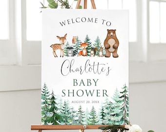 May include: A baby shower welcome sign on a wooden easel. The sign features forest animals and text that reads "Welcome to Charlotte's Baby Shower" with the date. The design includes watercolor trees and a deer, fox, and bear.