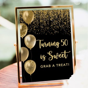 May include: A black and gold sign with gold balloons and glitter. The sign reads "Turning 50 is Sweet Grab a Treat!"