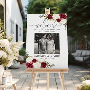 May include: Welcome sign for a 50th anniversary celebration with a photo of the couple, burgundy and white flowers, and the text "Welcome to the 50th Anniversary Celebration of Barbara & Frank August 23, 1975".