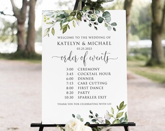 May include: A white wedding sign with green foliage and watercolor accents. The sign reads "Welcome to the wedding of Katelyn & Michael 03.25.2023 order of events" and lists the wedding day schedule.