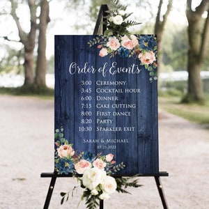 May include: A blue wooden sign with a floral design and the text "Order of Events" with a wedding schedule. The sign is on an easel and has the names Sarah & Michael and the date 03.25.2025.