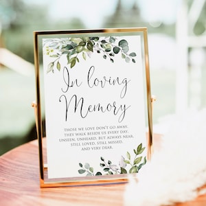 May include: A framed sign with a white background and green foliage border. The sign reads "In loving memory" and includes a quote about those we love who are gone but not forgotten.
