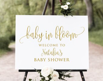 May include: White sign with gold lettering on an easel. The sign reads "baby in bloom" and "Welcome to Natalia's Baby Shower".