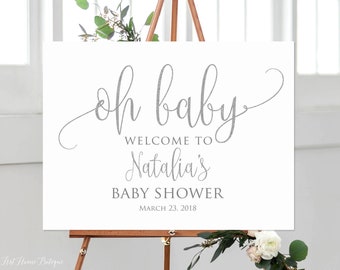 May include: White welcome sign with the text "Oh baby" in a silver glitter font. The sign also includes the text "Welcome to Natalia's Baby Shower March 23, 2018".
