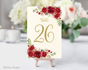 May include: Table number 26 with a gold font and a floral design with red roses and green leaves on a white background.