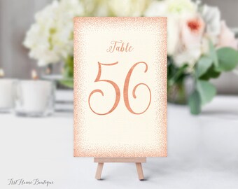May include: A white table number card with a rose gold glitter border and the text "Table 56" in rose gold script.