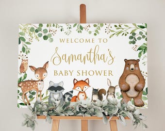 May include: Welcome to Samantha's Baby Shower sign with a woodland theme. The sign features a brown bear, a fox, a deer, a raccoon, a squirrel, and a rabbit. The sign is decorated with green leaves and branches.