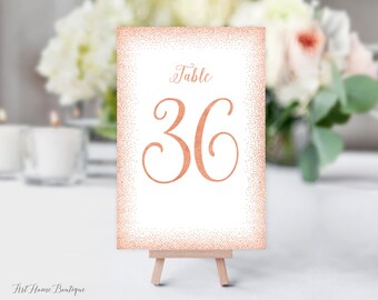May include: Rose gold table number card with a white background and a glitter border. The card says "Table 36" in a cursive font.