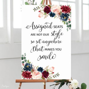 May include: A white sign with a floral border and the text "Assigned seats are not our style so sit anywhere that makes you smile".