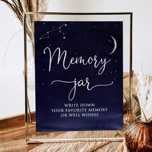 Peut inclure: Panneau encadré avec un fond bleu foncé, avec une écriture blanche qui dit "Memory Jar". Le panneau comprend une constellation et un croissant de lune. Le texte en dessous dit "Écrivez votre souvenir préféré ou vos bons vœux."