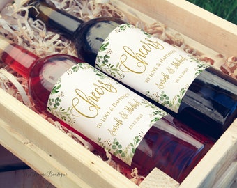 Könnte beinhalten: Zwei Weinflaschen mit personalisierten Etiketten in einer Holzkiste. Die Etiketten zeigen ein Blattdesign und den Text "Cheers to love and happiness" mit den Namen "Sarah & Michael" und dem Datum "10.12.2023".
