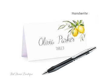 May include: White place card with the name "Olivia Parker" and "Table 3" in black script, decorated with a watercolor lemon and leaf design. A black pen rests on the table. The word "Handwrite" is above the place card.