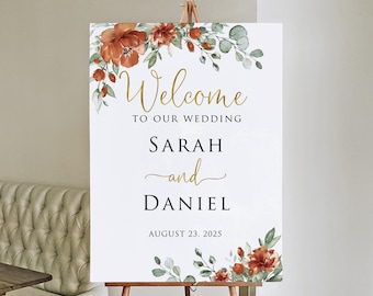 May include: A white wedding welcome sign on a wooden easel. The sign features gold script that reads "Welcome to our wedding" above the names "Sarah and Daniel" and the date "August 23, 2025". Floral accents in rust and green adorn the top and bottom.