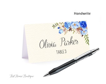 Può includere: Un segnaposto bianco con un design floreale blu ad acquerello. Il testo "Olivia Parker" e "Tavolo 3" è stampato sulla carta. È inclusa una penna nera.
