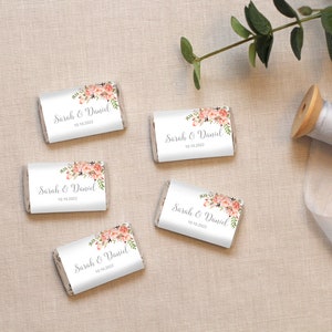 May include: Five white chocolate bar wrappers with pink floral designs and the text "Sarah & Daniel" and the date "10.10.2022".