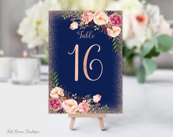 May include: A navy blue table number card with a rose gold glitter background and floral design. The card says "Table 16" in rose gold lettering.