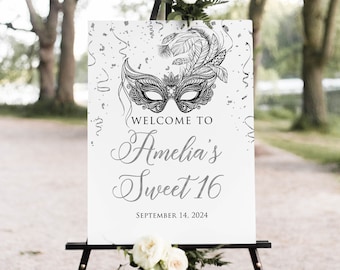Könnte beinhalten: Ein weißes Schild auf einer schwarzen Staffelei mit dem Text "Welcome to Amelia's Sweet 16" und dem Datum 14. September 2024. Das Schild zeigt ein dekoratives Masken-Design und ist mit weißen Blumen und Grün geschmückt.