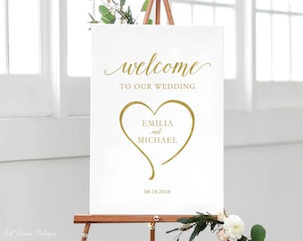 May include: White wedding welcome sign with gold lettering. The sign says "Welcome to our wedding" with a gold heart that says "Emilia and Michael" and the date "08.18.2018".