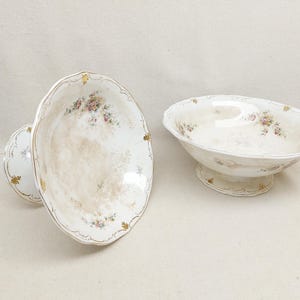 May include: Two antique porcelain serving bowls. One is a pedestal bowl, and the other is a shallow bowl. Both have a cream-coloured background with floral and gold accents. The pedestal bowl is approximately 25 cm in diameter.