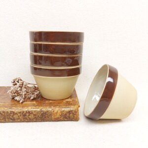May include: Set of five brown and beige ceramic bowls. The bowls are stacked on top of each other, with the top bowl being the only one that is not fully visible. The bowls have a brown rim and a beige interior.