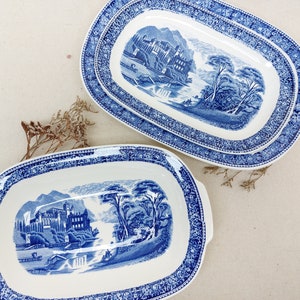 Puede incluir: Dos platos ovalados de servir azules y blancos con una escena de castillo azul y blanco. Los platos tienen un borde decorativo azul y blanco.
