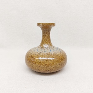 Könnte beinhalten: Eine kleine Keramikvase mit bauchigem Unterteil und engem Hals. Die Oberfläche ist mit einer gesprenkelten, beigen und braunen Glasur versehen, die feine blaue Punkte auf dem runden Körper aufweist. Das Finish ist glänzend und reflektiert Licht.