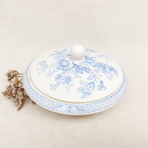 May include: A white ceramic dish with a blue floral pattern and a lid. The dish has a scalloped edge and a knob on the lid.