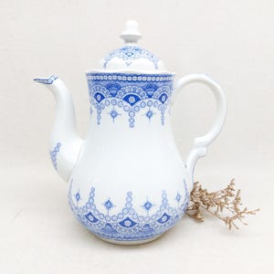 Peut inclure: Théière en porcelaine blanche avec un motif floral bleu. La théière a un bec verseur incurvé, une anse et un couvercle avec un petit bouton. Le motif bleu présente un motif répétitif de cercles et de formes florales.
