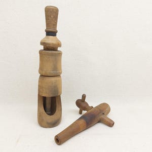 Pode incluir: Um conjunto vintage de torneira e saca-rolhas de vinho em madeira. O saca-rolhas é alto e cilíndrico, com uma pega e uma faixa preta. A torneira tem um bico e uma pega. Ambos os artigos são feitos de madeira castanha clara.