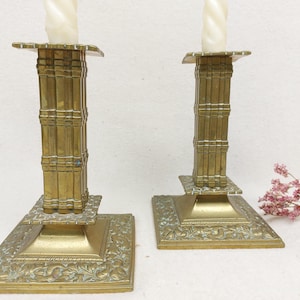 Può includere: Due portacandele in ottone decorati con un designo decorativo. Ogni portacandele ha una base alta e sottile e una parte superiore larga e piatta. Le candele non sono incluse.