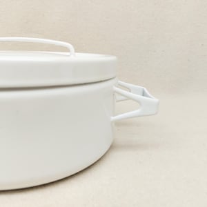 Puede incluir: Una olla de esmalte blanco con tapa y asa. La olla tiene forma redondeada con un asa en la tapa y dos asas laterales. La olla es de metal y tiene un acabado brillante. Está diseñada para cocinar.