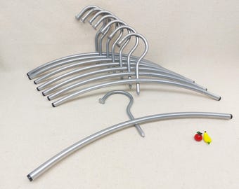 May include: A set of silver metal hangers with a curved shape. The hangers are arranged in a stack, with the hooks facing up. There are two small decorative fruit charms on the table.