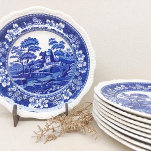 Op de afbeelding: Een set blauwe en witte keramische dinerborden met een bloemenpatroon en een landschapsscène met een brug en bomen.
