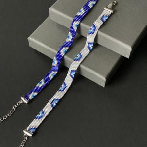 Könnte beinhalten: Zwei Perlenarmbänder mit einem blauen und weißen bösen Augenmuster. Die Armbänder liegen auf einer grauen Oberfläche.