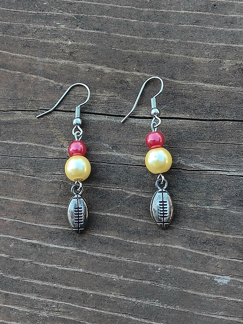 May include: A pair of silver earrings with red and yellow beads and a football charm.