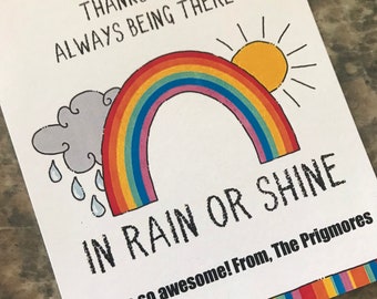 Op de afbeelding: Een witte kaart met een regenboog, zon en wolk illustratie. De kaart zegt "Bedankt dat je er altijd bent, regen of zonneschijn. Je bent zo geweldig! Van de Prigmores".