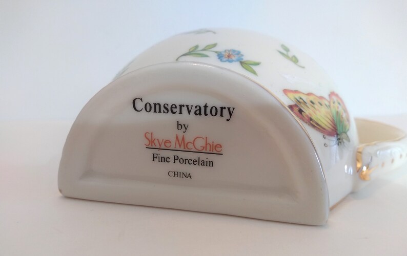May include: A white porcelain butter dish with a gold trim and a butterfly design. The dish is labelled "Conservatory by Skye McGhie Fine Porcelain CHINA".