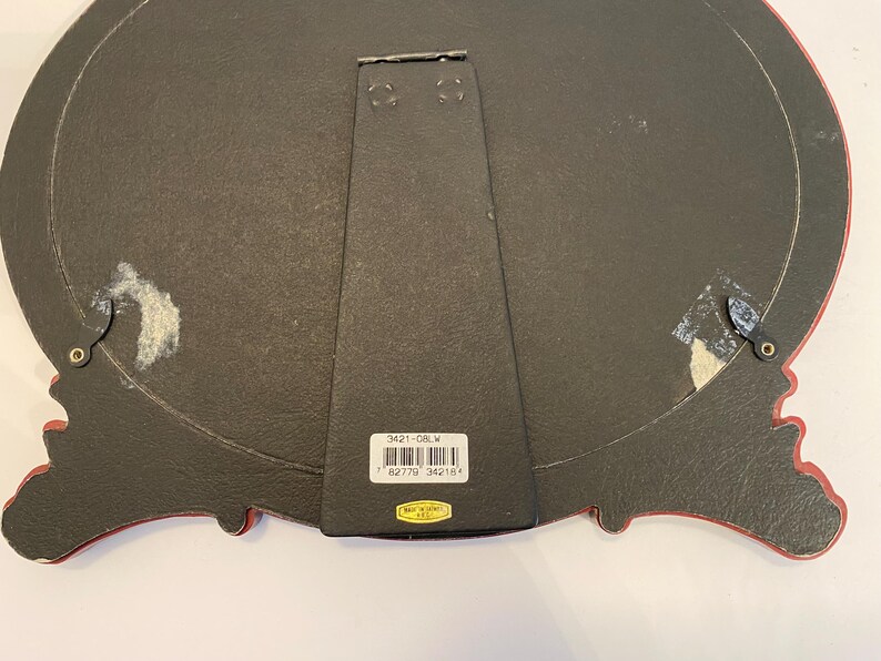 May include: Black oval picture frame with a red and gold ornate design. The back of the frame has a label with the text "3421-08-W" and a barcode.