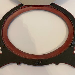May include: A red oval picture frame with a black outer edge and ornate detailing. The frame is made of wood and has a matte finish.