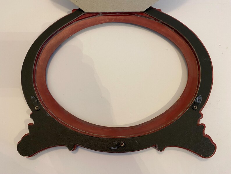 May include: A red oval picture frame with a black outer edge and ornate detailing. The frame is made of wood and has a matte finish.