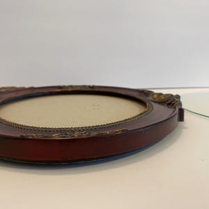 May include: A dark red oval picture frame with a gold trim and ornate details. The frame is empty and ready for a photo.