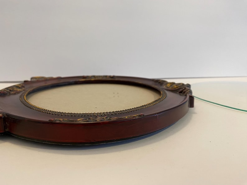 May include: A dark red oval picture frame with a gold trim and ornate details. The frame is empty and ready for a photo.