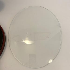 May include: A clear glass circle with a slightly chipped edge. The glass is smooth and reflective.